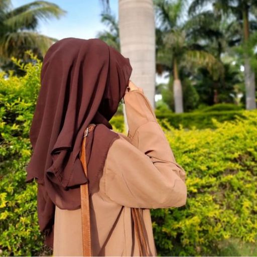  A woman in a brown hijab standing in front of palm trees.