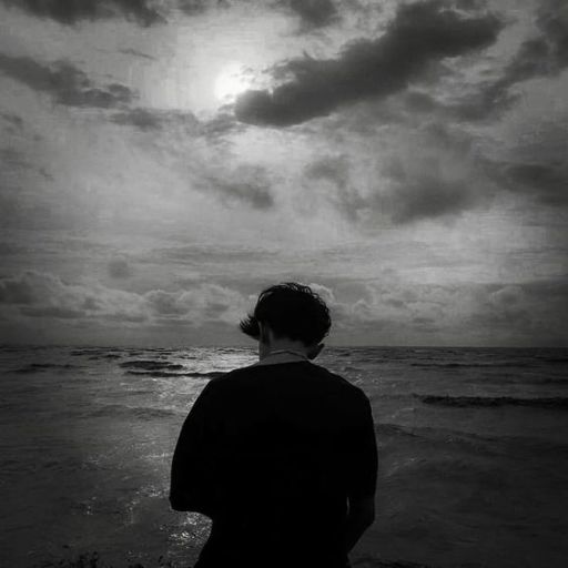 a black and white photo of a person looking out at the ocean