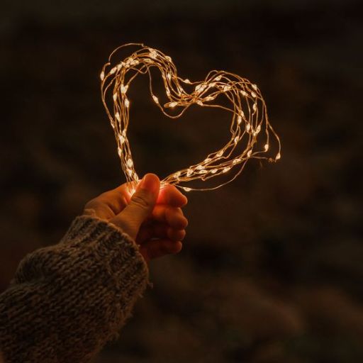 A hand holding a string of lights shaped like a heart against a dark background