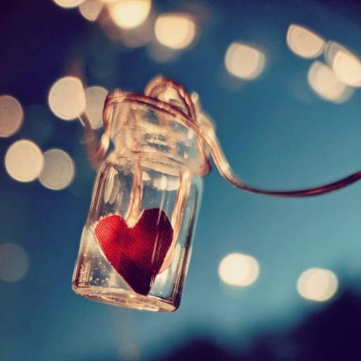 A red heart inside a small glass jar with bokeh lights in the background