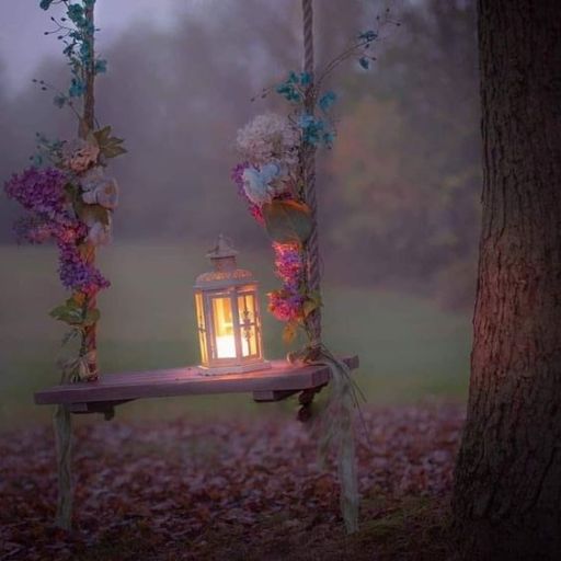 Swing adorned with flowers and a lit lantern at dusk beside a tree