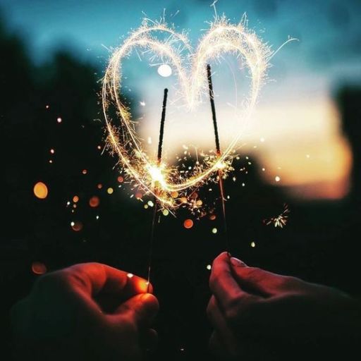 Two hands holding sparklers forming a heart shape with a twilight sky in the background