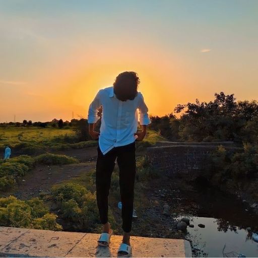 a man standing on a ledge with the sun setting in the background