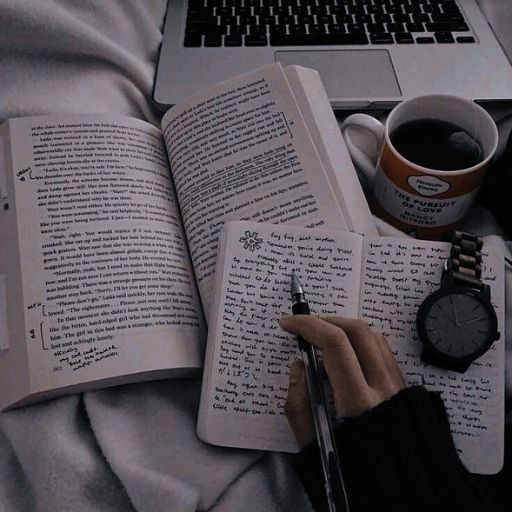 a person holding a pen and writing on a book next to a laptop