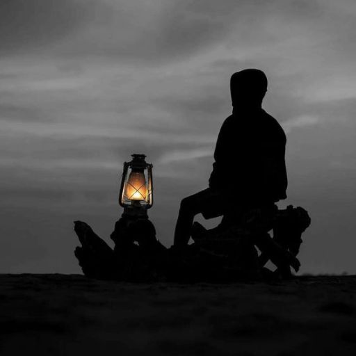 a person sitting in the sand next to a lantern