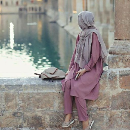 a woman in a hijab sitting on a ledge next to a body of