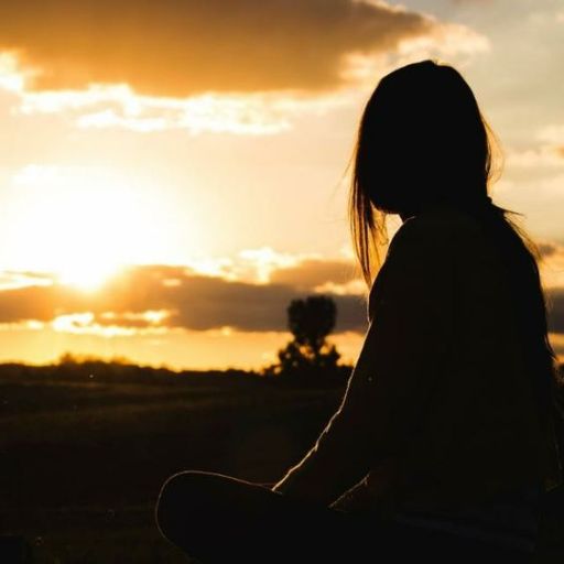 a woman sitting in the grass watching the sun go down