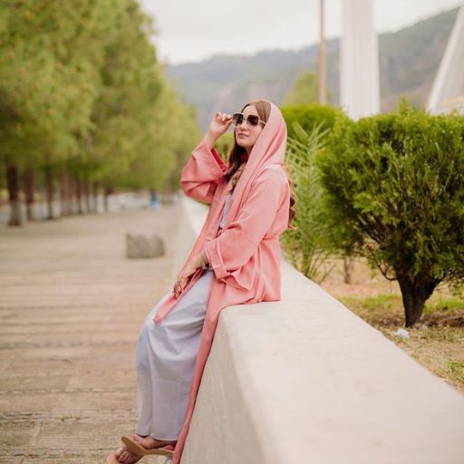 a woman sitting on a wall wearing a pink coat