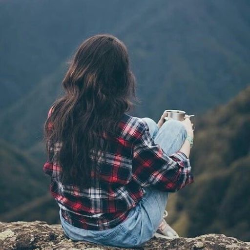 a woman sitting on top of a mountain holding a cup of coffee