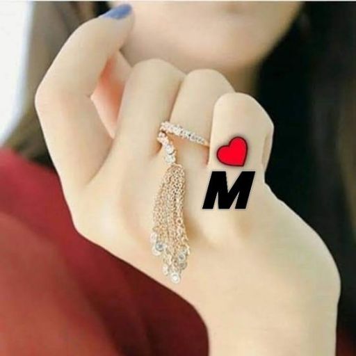 A close-up of a hand with a tassel earring between fingers, marked with a red heart and letter 'M'