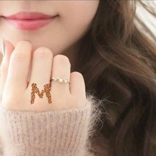 A close-up of a woman's lower face and hand, wearing a pink sweater and delicate rings, touching her chin