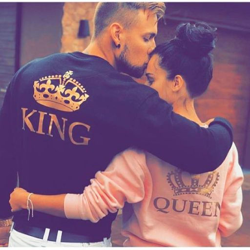 A couple dressed in matching king and queen sweatshirts, smiling together in a cozy setting, showcasing their playful bond