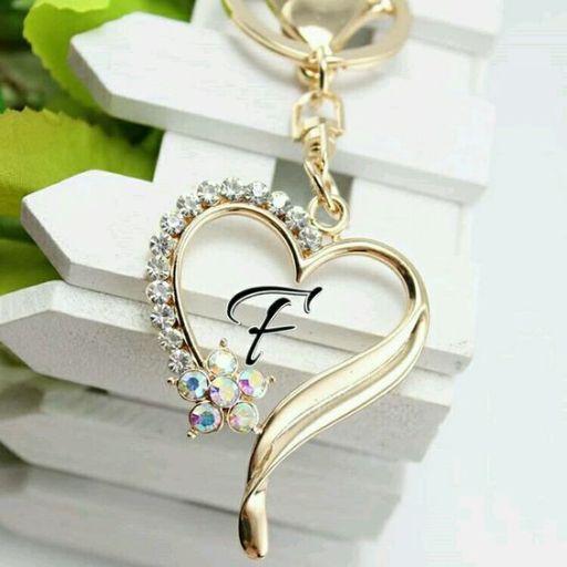 A gold-tone heart-shaped keychain with rhinestones and a letter _F_ inside, on a white surface