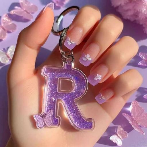 A hand holding a glittery purple keychain with the letter 'R' surrounded by small floral embellishments