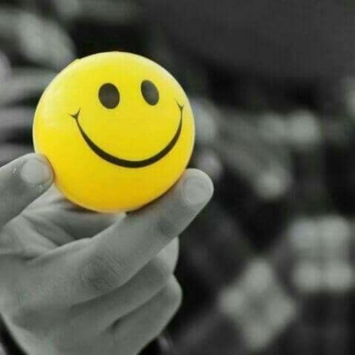 A hand holding a yellow smiley face badge, with a selective color effect on a grayscale background