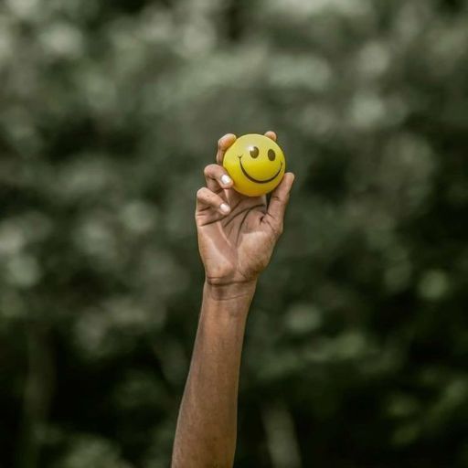 A hand holding up a yellow smiley face ball against a blurred green background