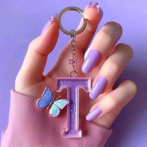 A hand with purple nails holds a glittery 'T' keychain with a butterfly