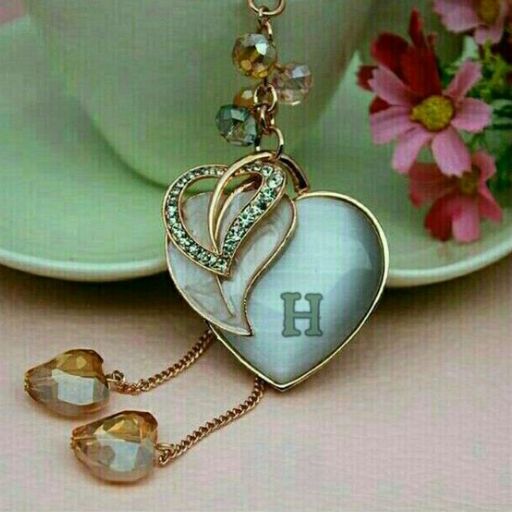 A heart-shaped keychain with crystals and an engraved letter _H_ against a teacup and flowers background