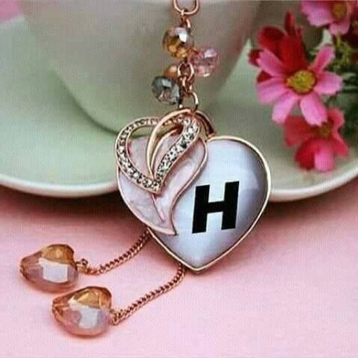 A heart-shaped pendant with the letter _H_ on a pink background, adorned with crystals and flowers nearby