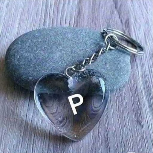 A keychain with a clear heart-shaped pendant with the letter _P_ inside, resting on a gray stone and a wooden surface