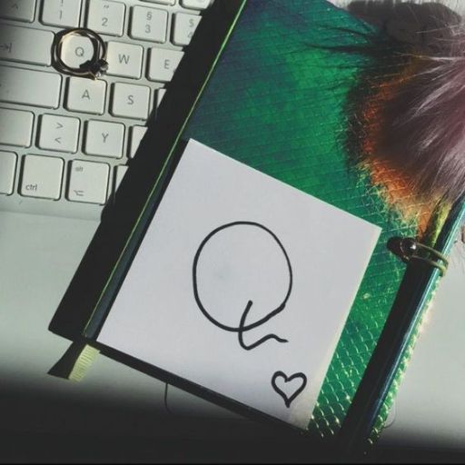 A notebook with a doodled letter Q and a heart on its cover, resting on a laptop keyboard