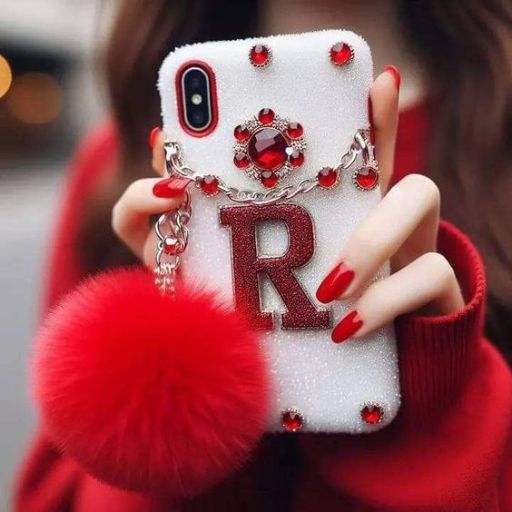 A person holding a sparkling phone case with a red letter _R,_ jewels, and a fluffy pom-pom, matching their red nails