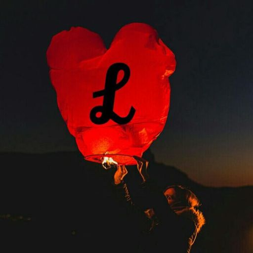 A person releasing a red heart-shaped lantern with a letter 'L' into the evening sky