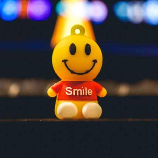 A smiling yellow figurine with a _Smile_ T-shirt against a bokeh light background