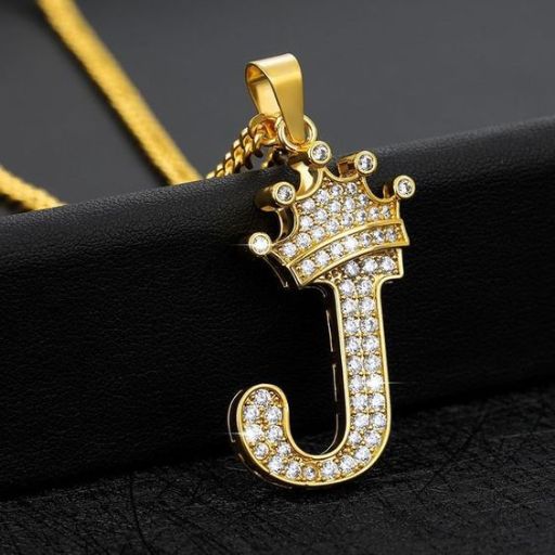 Gold letter 'J' pendant with crown and diamonds on a black surface