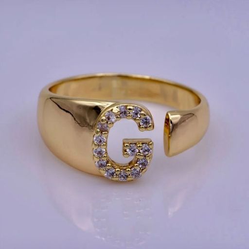 Gold signet ring with letter 'G' encrusted with diamonds on purple background