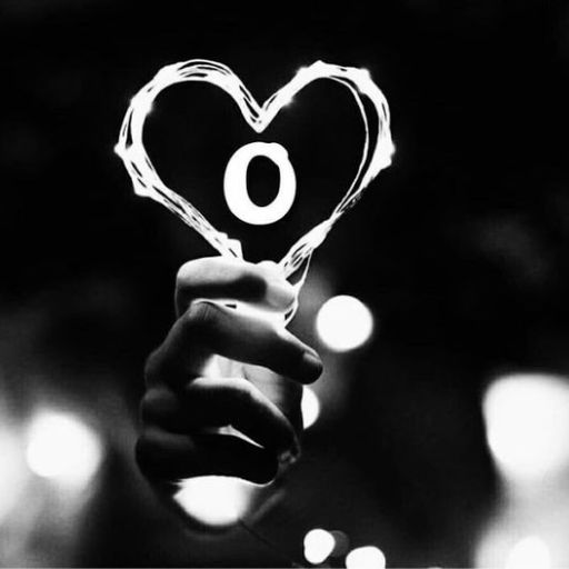 Hand holding a sparkler drawing a heart shape with circular light at the center against a bokeh background in black and white