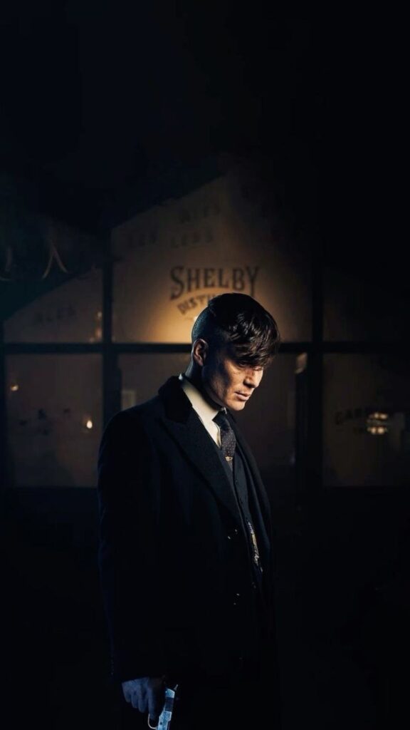 Man in a dark suit holding a razor, with _Shelby Company Ltd._ sign in the background