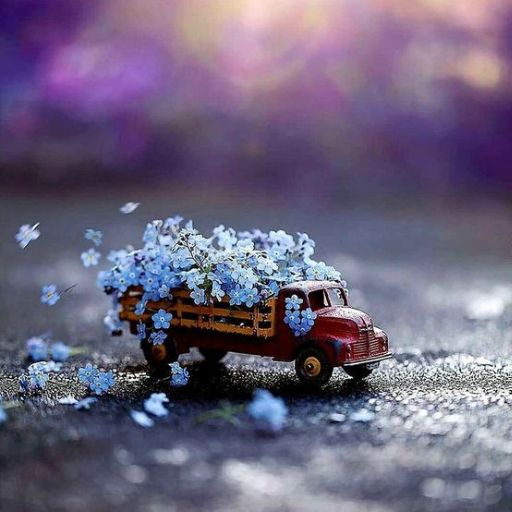 Miniature toy truck carrying blue flowers with petals scattered on a textured surface