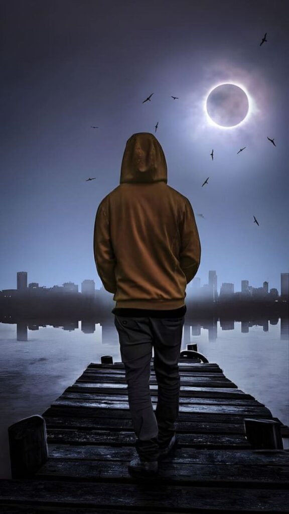 Person in hoodie standing on pier watching solar eclipse over city silhouette with birds flying