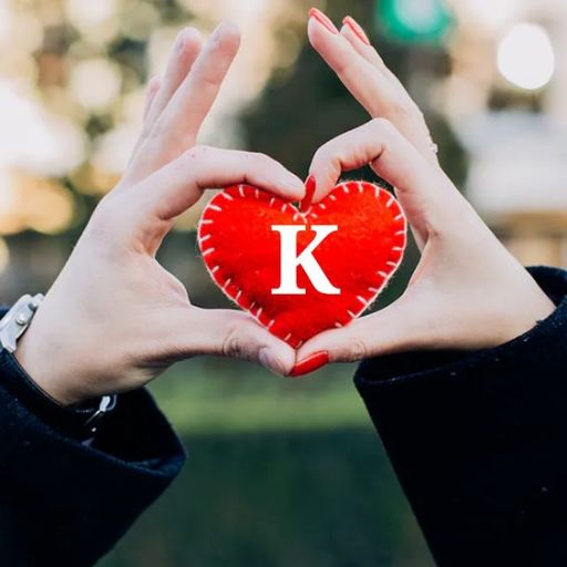 Two hands forming a heart shape around a red heart with a letter _K_ on it