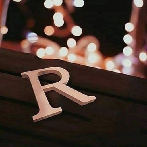 White letter 'R' on a dark surface with blurred lights in the background