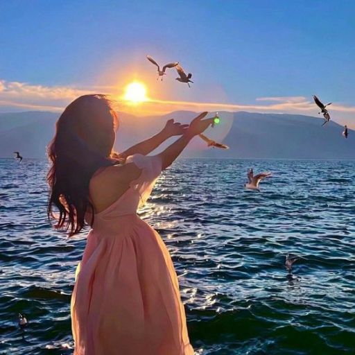 a girl in a pink dress looking at birds flying over the water