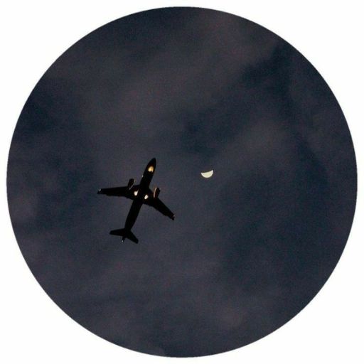 an airplane flying in the sky with a half moon in the background