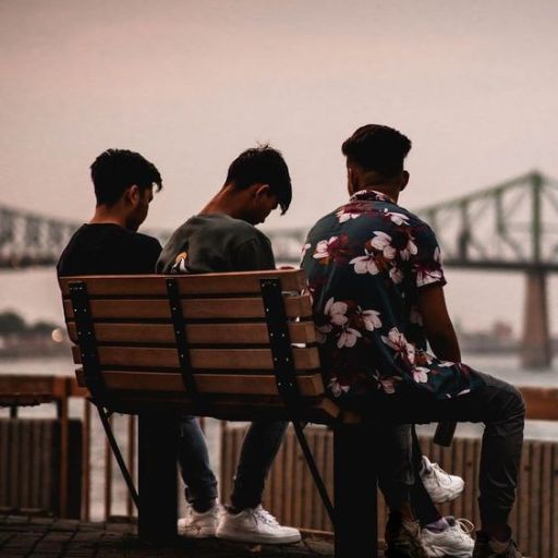 three men sitting on a bench near a body of water