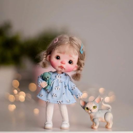 A child in a blue dress holding a toy with a cat figurine beside her, against a bokeh light background