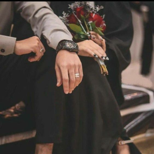 A close-up of a couple holding hands, the woman is holding a bouquet, both are dressed elegantly