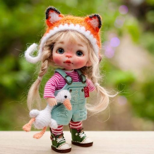 A doll with a fox hat and overalls holding a crochet toy, standing outdoors