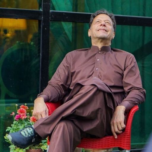 A person dressed in a brown traditional outfit sitting on a red chair, with flowers to the left