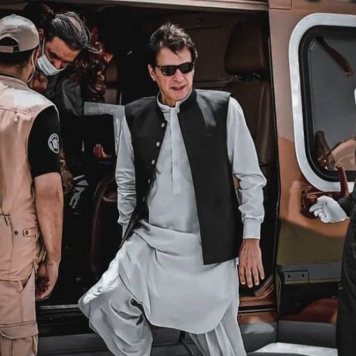 A person in traditional attire steps out of a helicopter, flanked by security personnel