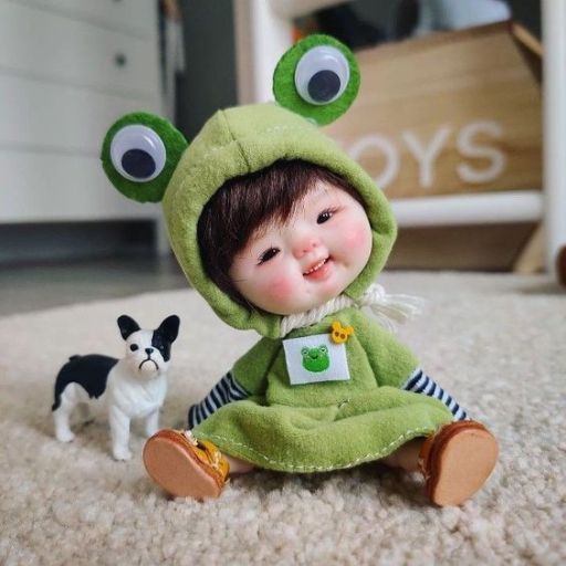 A plush toy frog in a green outfit sitting next to a small toy dog on a carpet