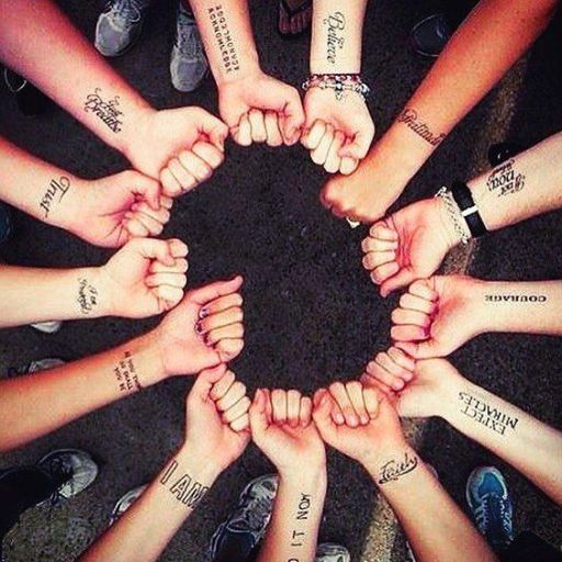 Circle of people holding fists together, tattoos and wristbands visible, top view on pavement