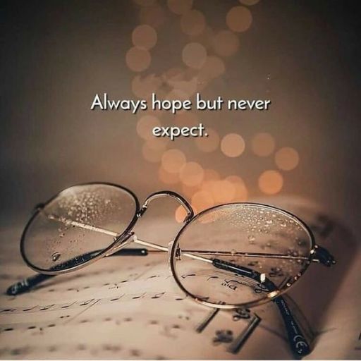 Eyeglasses with water droplets on a book with the phrase _Always hope but never expect._ Bokeh background