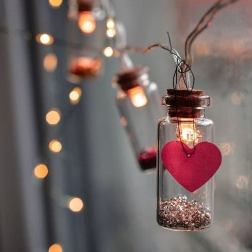 Glass jars with lights and a heart-shaped tag hanging against a blurred background of warm lights