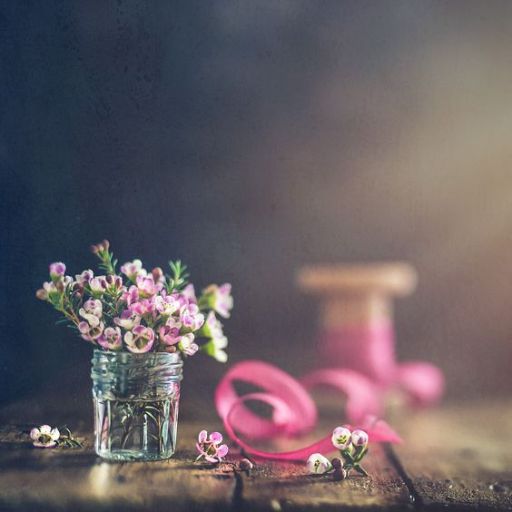 Jar of pink flowers with a spool of ribbon on a rustic wooden surface