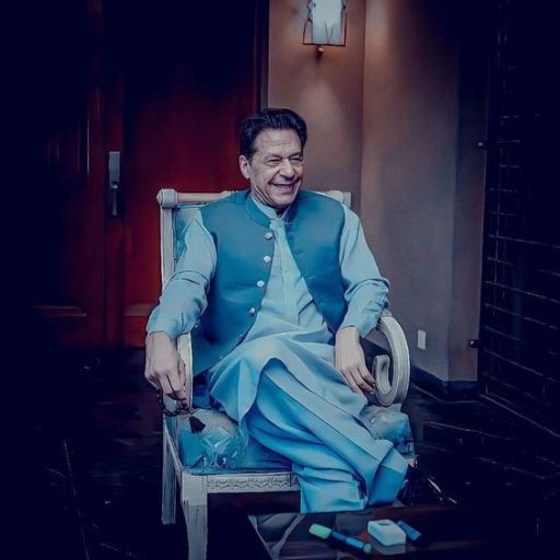 Man in traditional blue attire sitting on a chair with a hat in hand